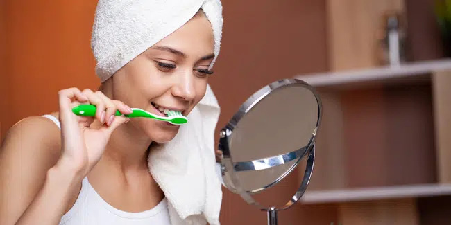 Woman brushing her teeth at home between professional teeth cleanings in Richardson, TX